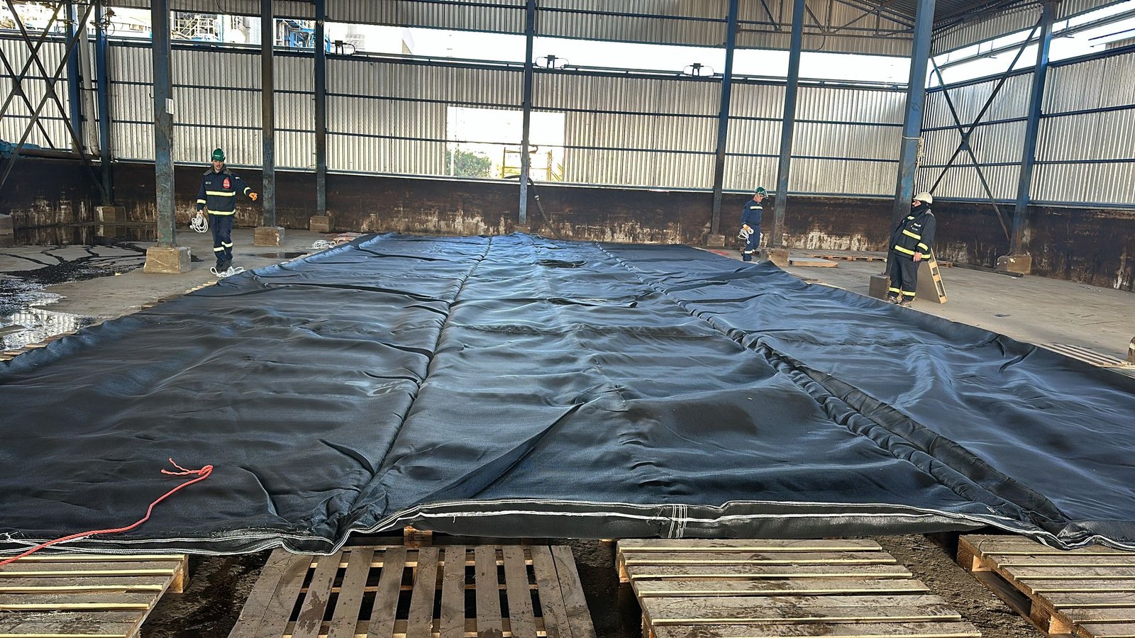 Atölyede paletler üzerine serilmiş geotekstil tüp ve çalışanlar.